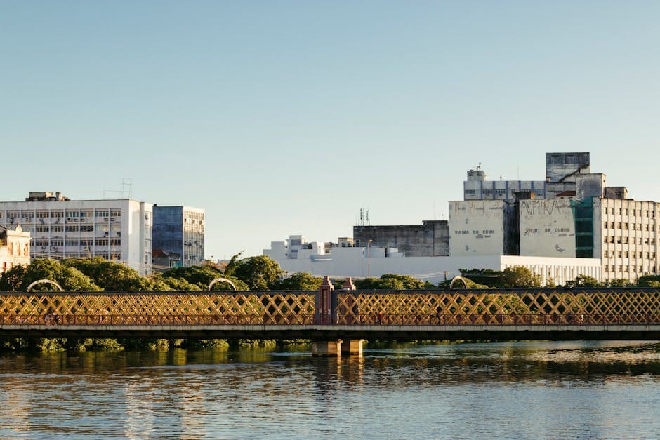 Serene view of a heritage bridge and urban skyline reflecting in calm waters during the day.