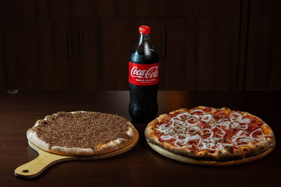 Two delicious pizzas with a bottle of Coca Cola on a wooden table for a casual meal.