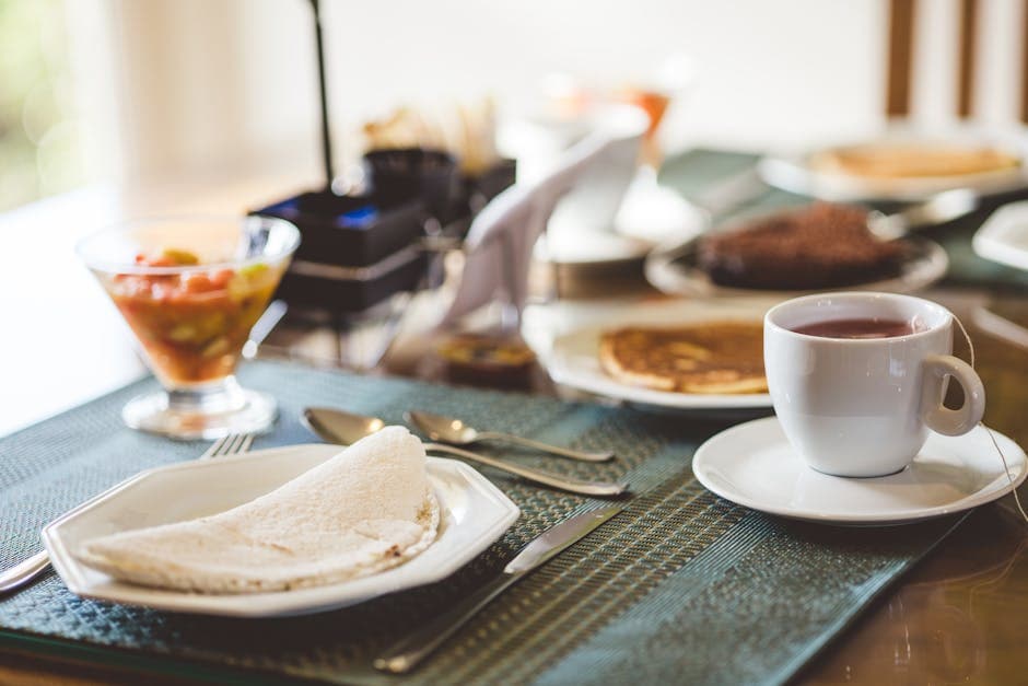 A cozy breakfast setting featuring tea, crêpes, and fruit salad on a neatly arranged table indoors.