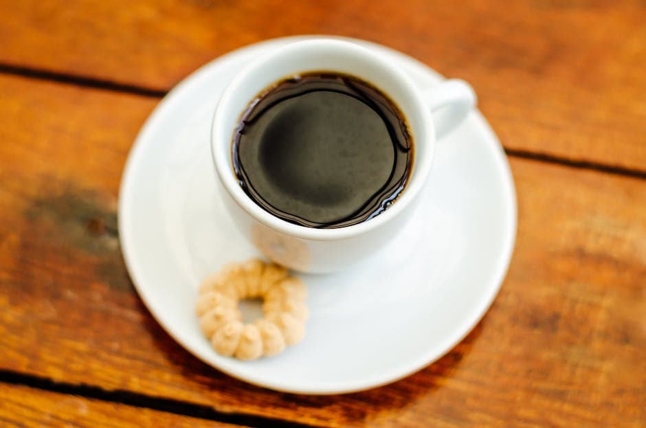 A steaming cup of black coffee with a cookie on a wooden table.