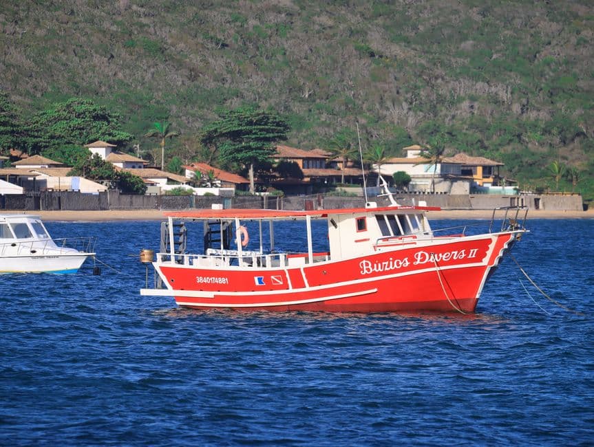 Vibrant red dive boat "Buzios Divers II" anchored near the scenic coastline of Buzios, Brazil.
