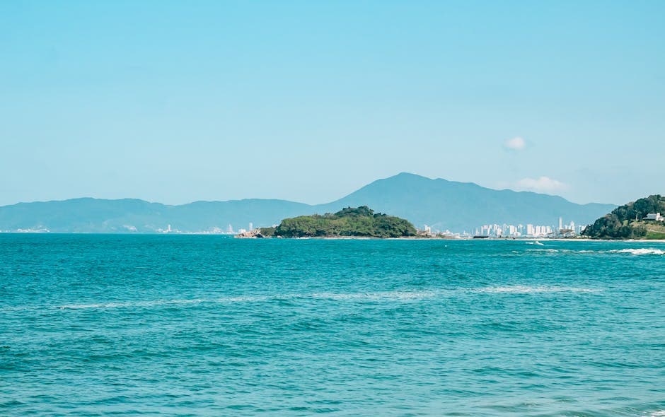 Beautiful seascape with clear blue waters, an island, and a distant city under a bright summer sky.