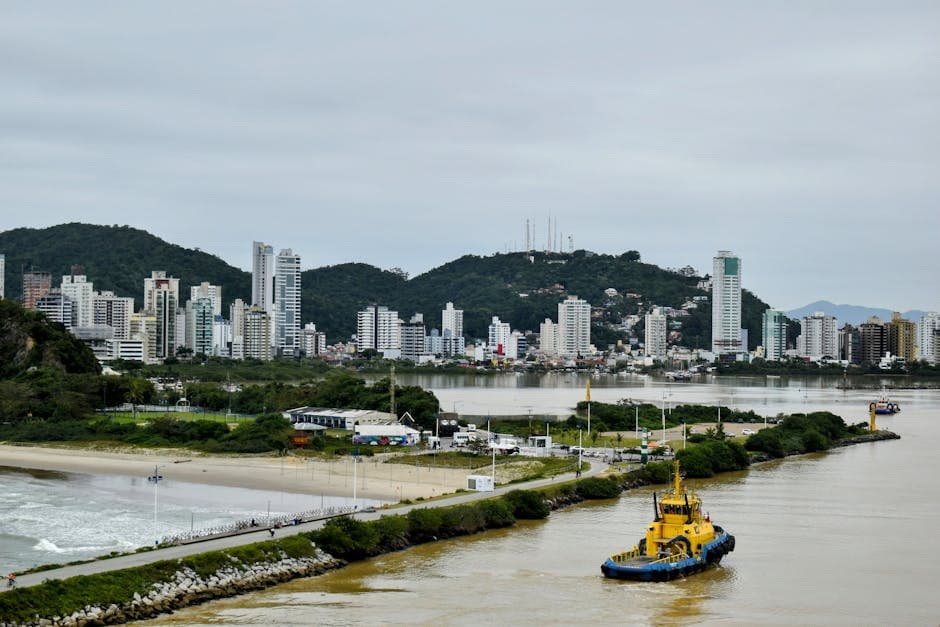 Skyscrapers of Navegantes, Brazil, overlooking a serene harbor with a vibrant yellow tugboat.