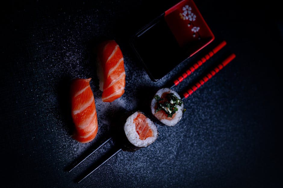 A vibrant display of salmon sushi and maki rolls with chopsticks and soy sauce, shot from above.