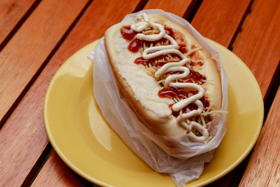 Savoury Brazilian hot dog with ketchup and mayonnaise on a yellow plate.