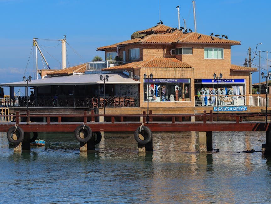 A waterfront building with a wooden pier and seating area under a clear blue sky.