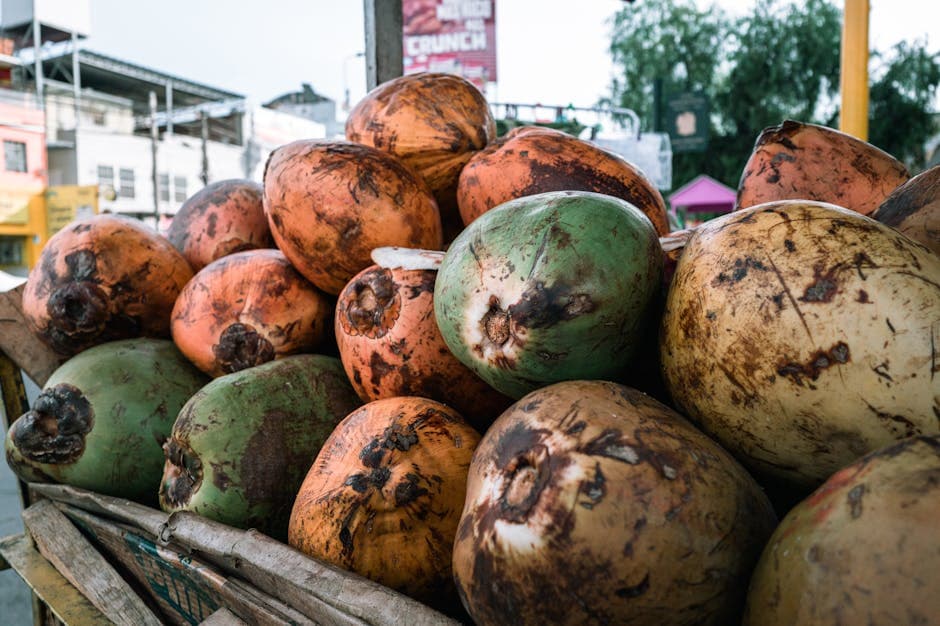 A stack of fresh coconuts displayed on a street vendor cart in a bustling market.