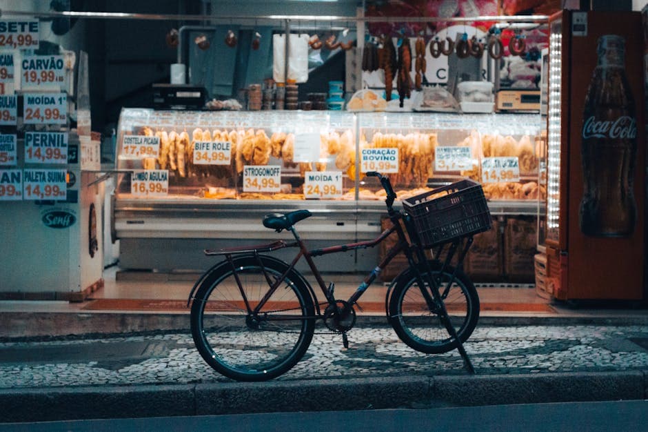 A bicycle parked outside a brightly illuminated shop in Curitiba at night, showcasing various market goods.