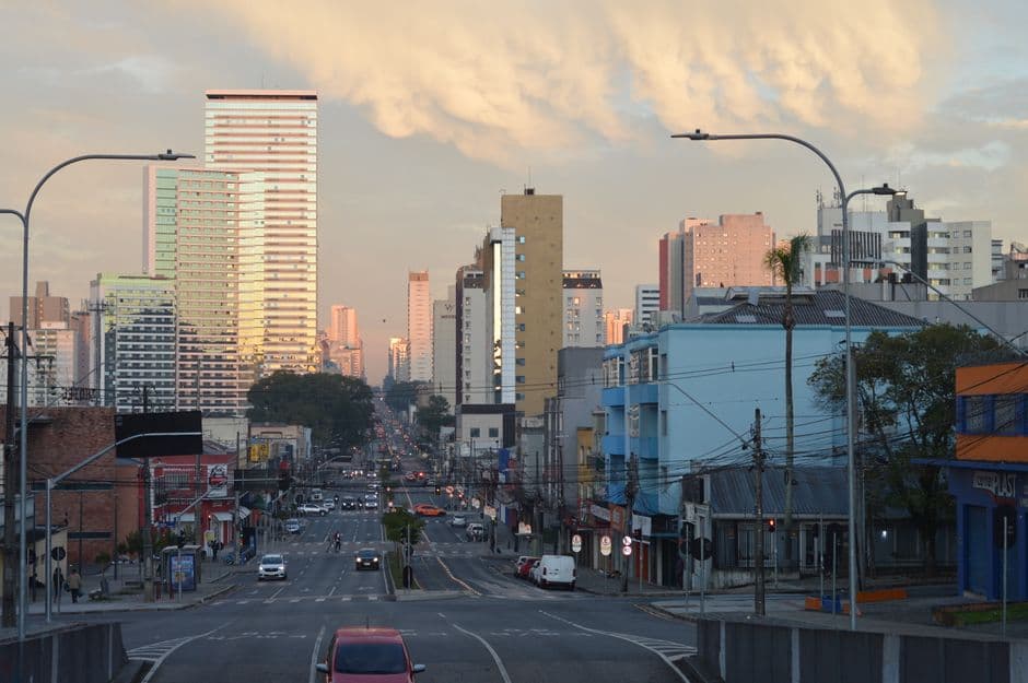 Urban skyline of Curitiba, Brazil, captured at sunset featuring high-rise buildings and city streets.
