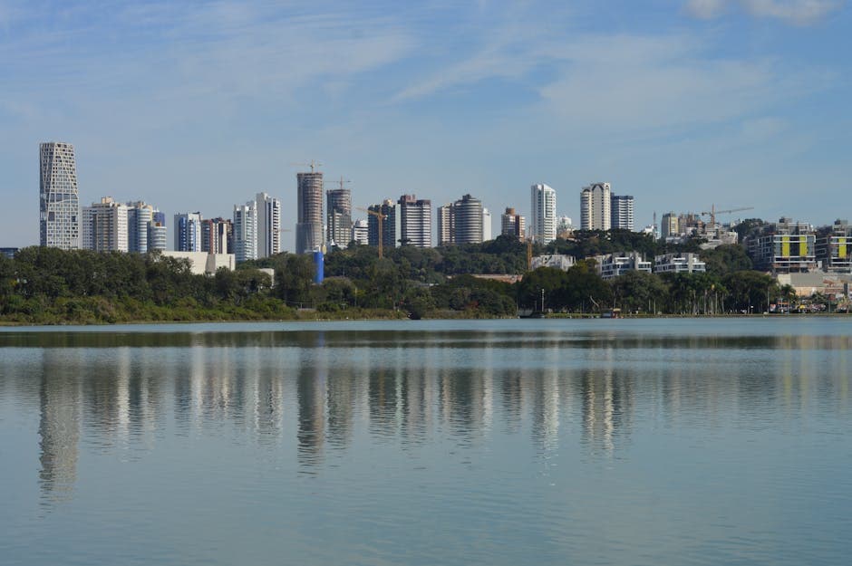 Skyline of Curitiba, Brazil, reflecting on a serene lake under a clear blue sky.