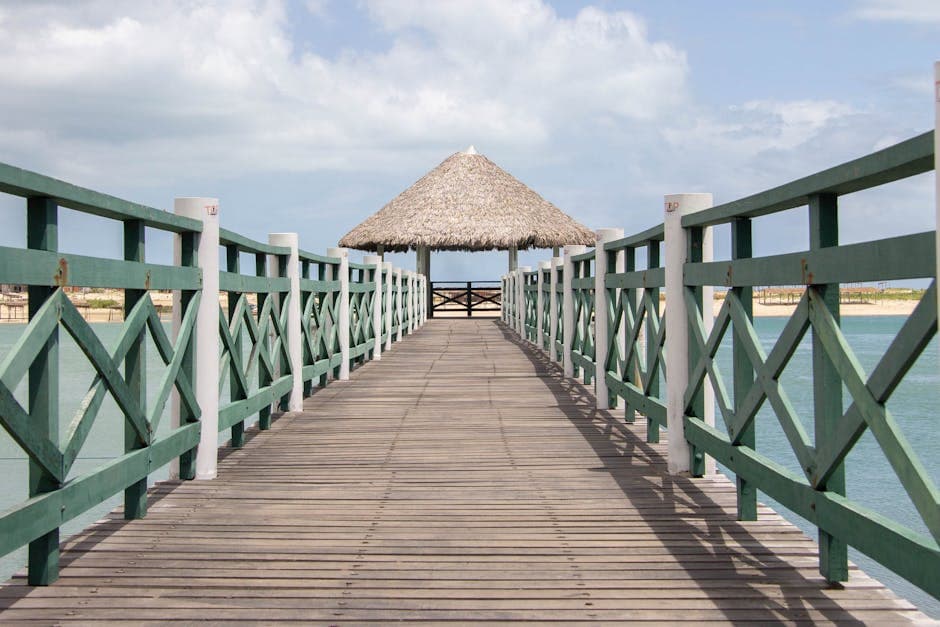 Wooden walkway with railings leading to a nipa hut over a serene lagoon in Brazil, perfect summer getaway.