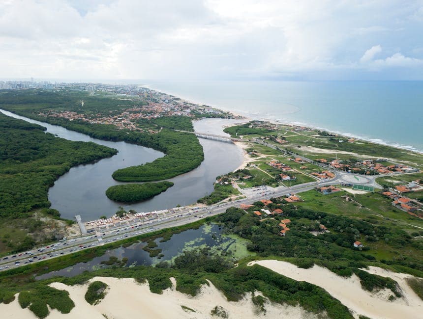 Aerial shot of Fortaleza's lush coastline, featuring winding river, dunes, and ocean.