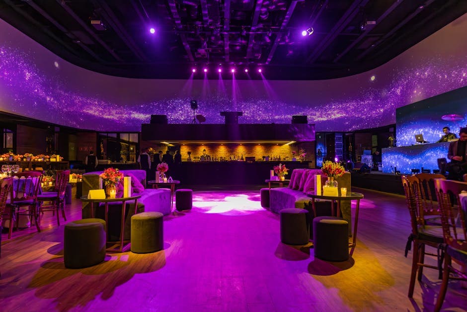 Elegant restaurant interior with purple lighting and stylish decor, featuring comfortable seating and floral arrangements.