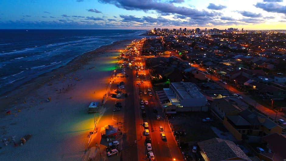 A stunning aerial view of Imbé Beach, Brazil, captured at dusk with vibrant city lights and ocean waves.