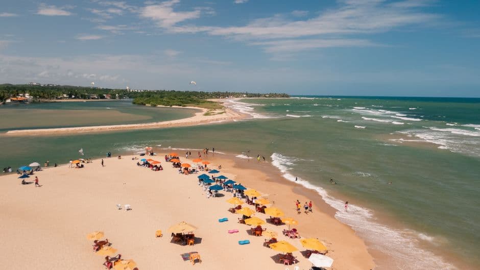 Aerial view of a vibrant beach in Lauro de Freitas, Bahia, showcasing colorful umbrellas and clear ocean waves.
