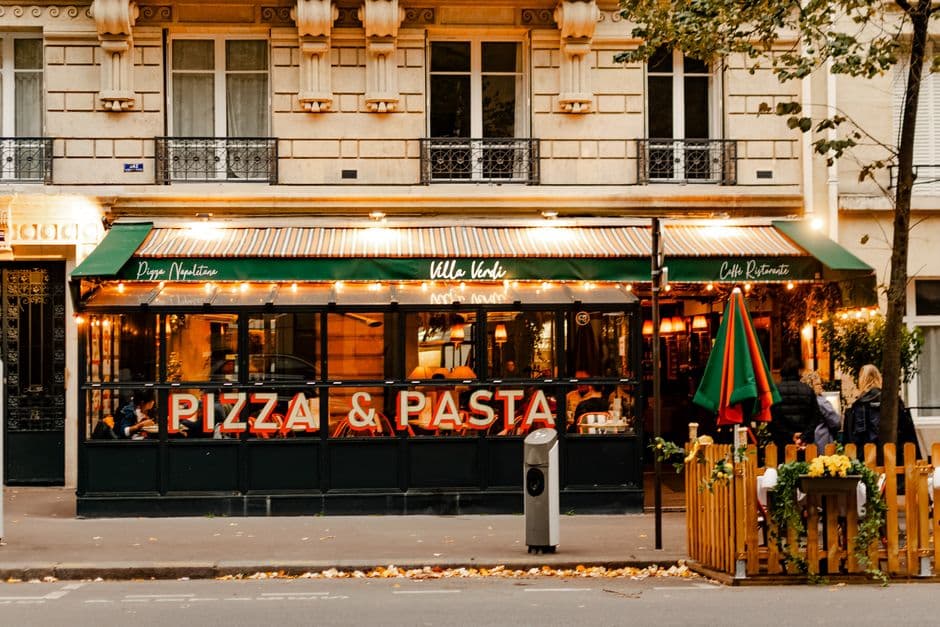 Cozy street view of a pizza and pasta restaurant with warm, inviting lighting.