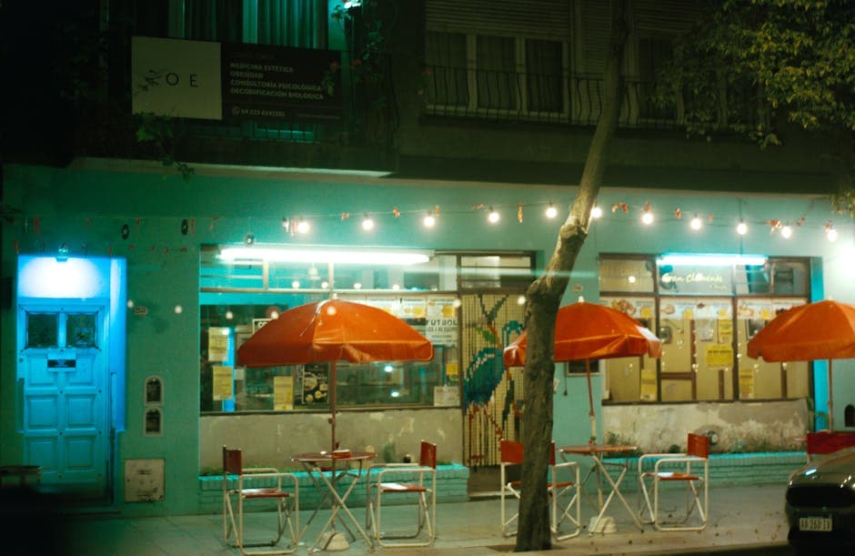Outdoor cafe with red umbrellas and string lights at night, cozy ambiance.