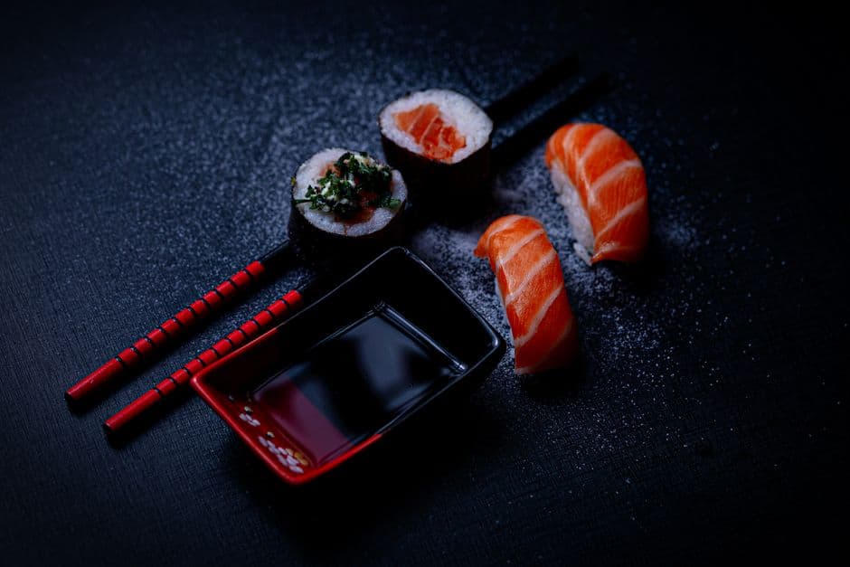 Artistic presentation of salmon sushi with soy sauce and chopsticks on a dark background.