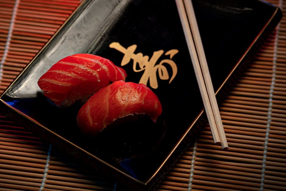 A close-up of two pieces of salmon sushi on a decorative plate with chopsticks.
