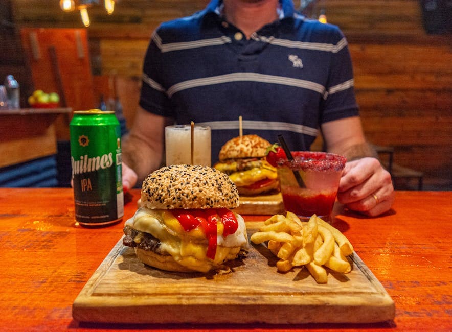 Mouthwatering burger, fries, and drinks on a wooden table in a cozy restaurant setting.
