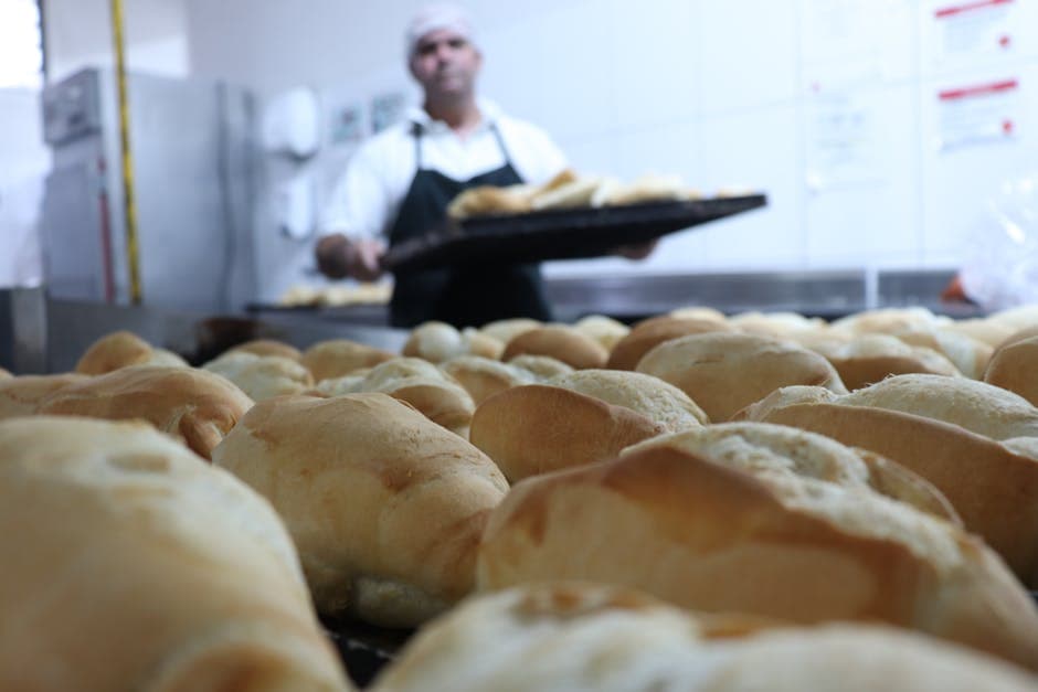 Close-up of freshly baked bread in a bakery kitchen, showcasing golden crusts and a baker in the background.