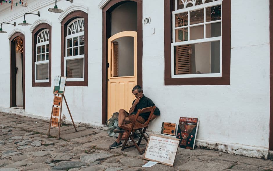 An elderly man sits reading outside a charming, historical building.