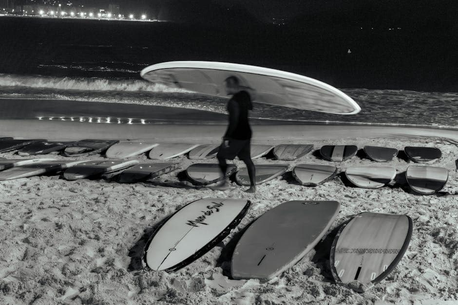 A surfer walks on a Rio de Janeiro beach at night, surrounded by surfboards, creating a serene beachside scene.