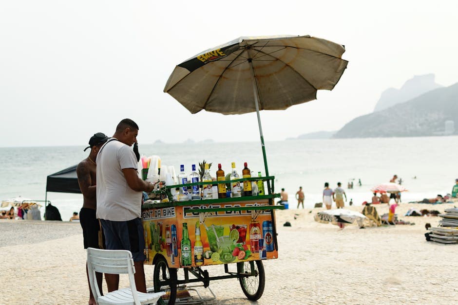 Street vendor on Rio beach selling drinks under an umbrella with ocean backdrop.