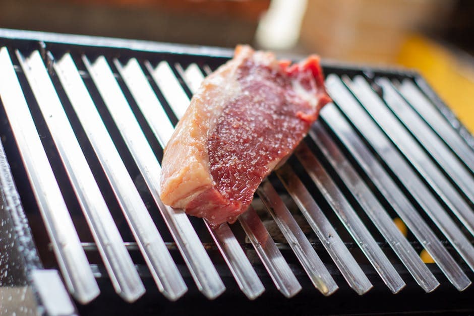 Close-up of a raw beef steak seasoned with salt on a grill grate in Recife, Brazil.
