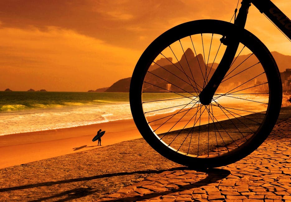 A striking sunset on a Brazilian beach with a bicycle wheel and surfer silhouette.