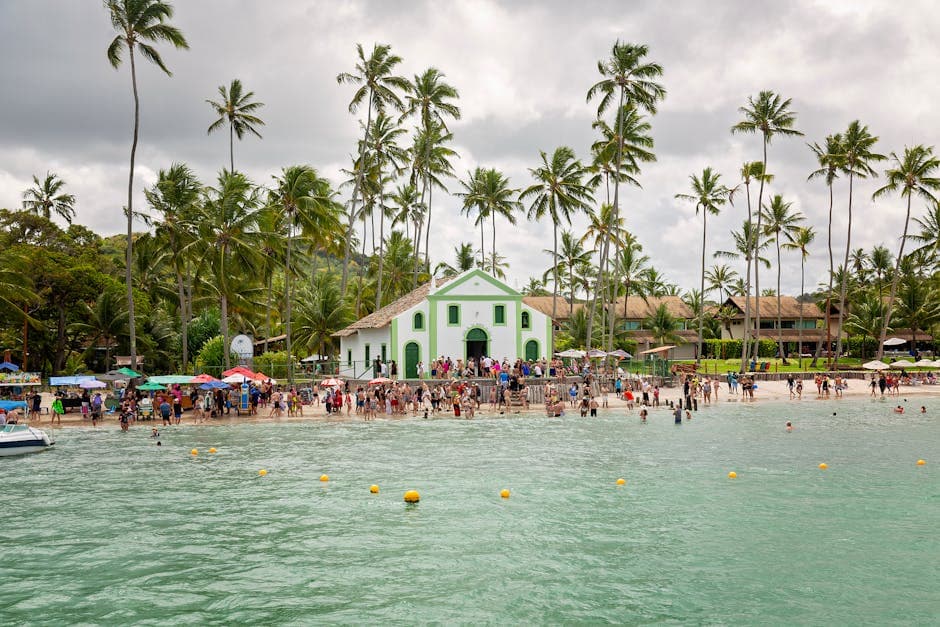 Bustling beach scene with Igreja de São Benedito and vibrant crowd under tall palm trees.