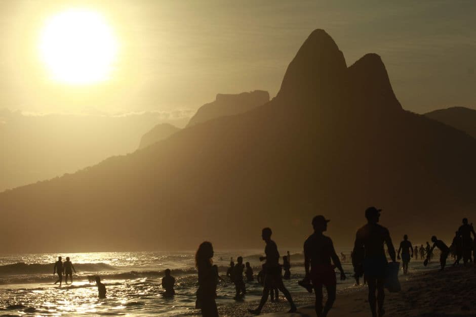 Silhouettes of people enjoying the beach at sunset with Rio's iconic mountains in the background.
