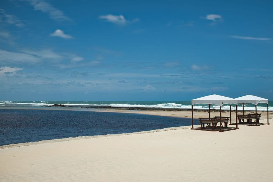 Tranquil beach scene with gazebos at Barra do Cunhaú, Brazil, perfect for relaxation.