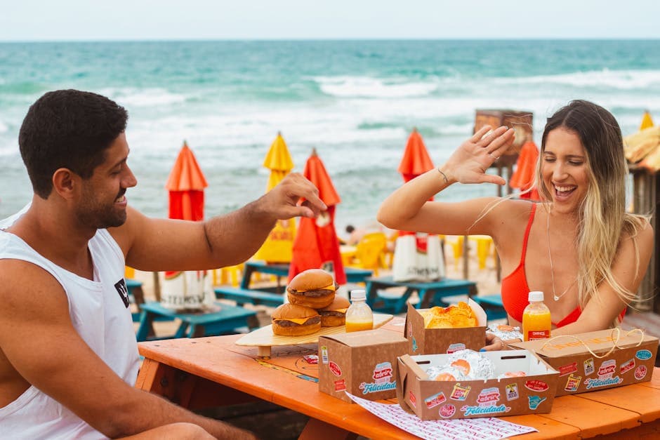 A happy couple enjoying burgers and drinks at a beachside picnic scene.