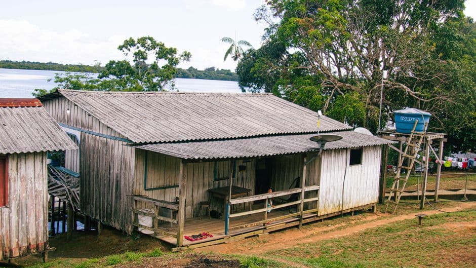 A rustic house by the Amazon River surrounded by lush greenery and calm water.