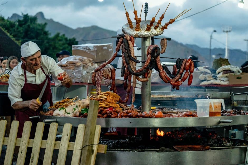 Elderly man grilling sausages and meats at an outdoor market in Santa Cruz, Tenerife.