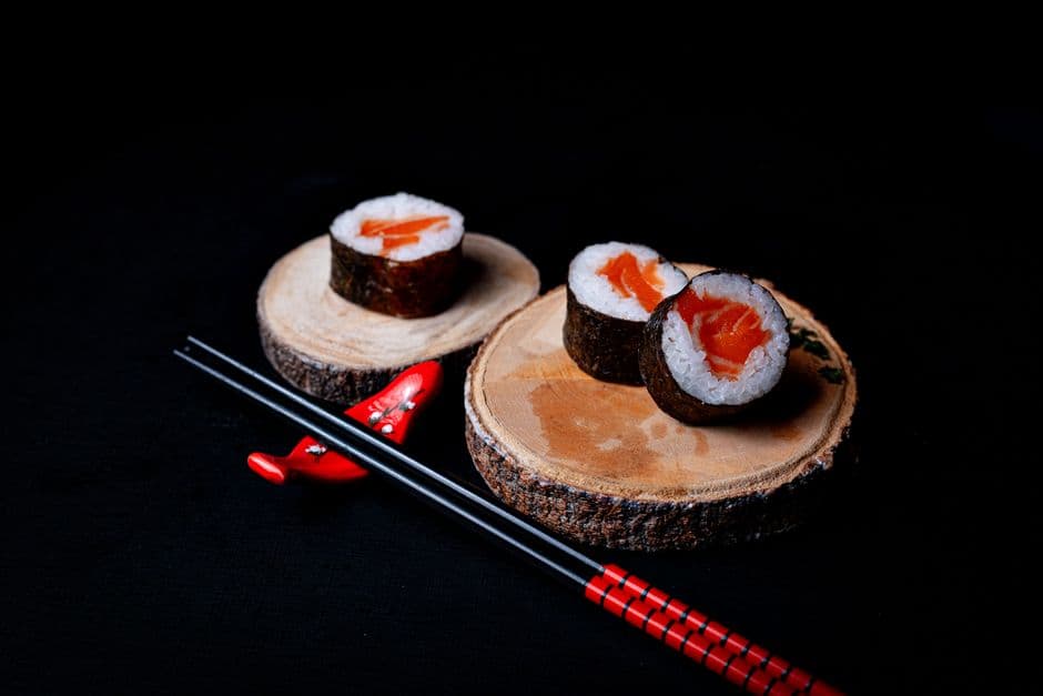 Close-up of salmon sushi rolls on wooden placemats with chopsticks, showcasing Japanese culinary artistry.