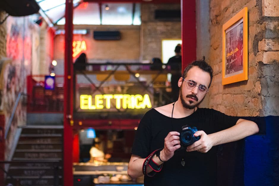 Portrait of a stylish photographer in a vibrant São Paulo bar with neon lights.