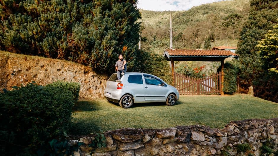 A man sits on a parked car enjoying a scenic landscape in São Bento do Sapucaí, Brazil.
