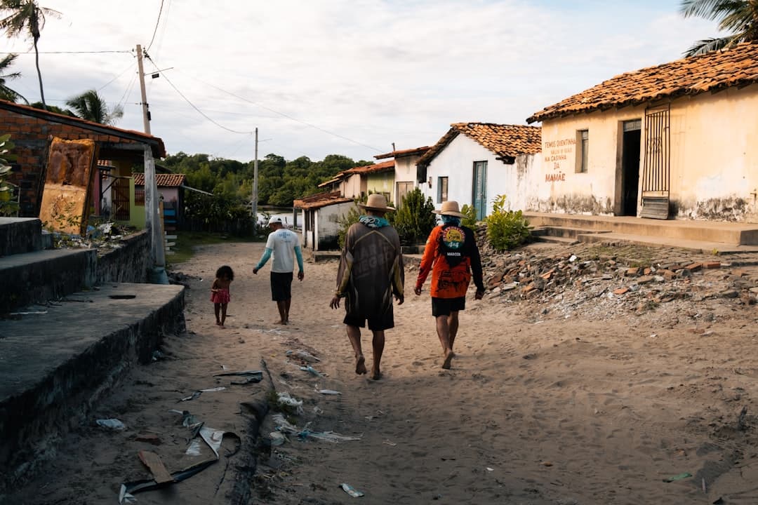 a group of people walking on a dirt road between buildings