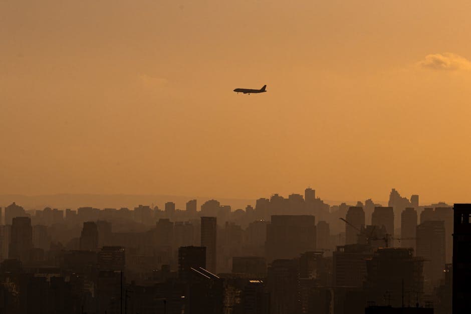 A silhouette of an airplane flying over Sao Paulo's skyline during a golden sunset.