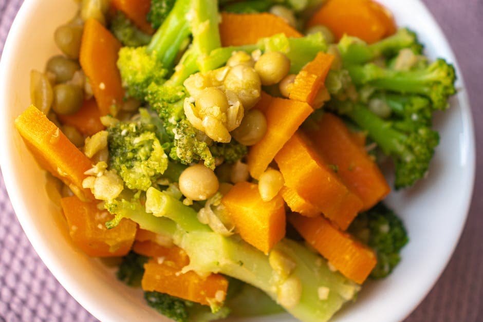 Colorful mix of steamed carrots, broccoli, and peas in a white bowl.