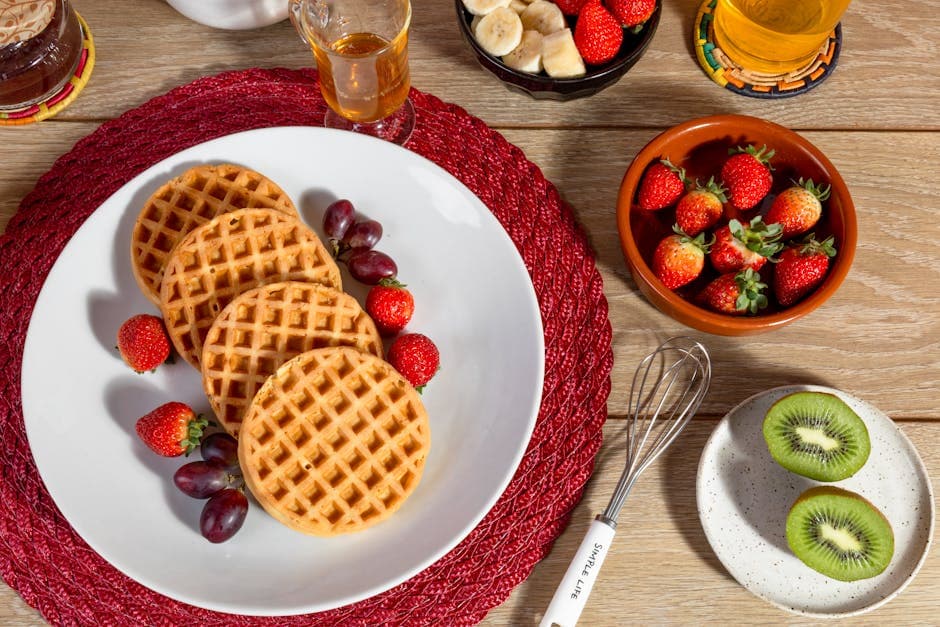 A vibrant breakfast spread featuring waffles, strawberries, grapes, bananas, and kiwi.