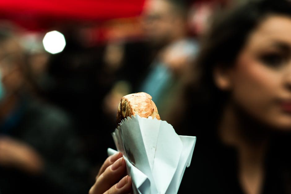 A hand holding a wrapped snack in a bustling São Paulo street food scene.