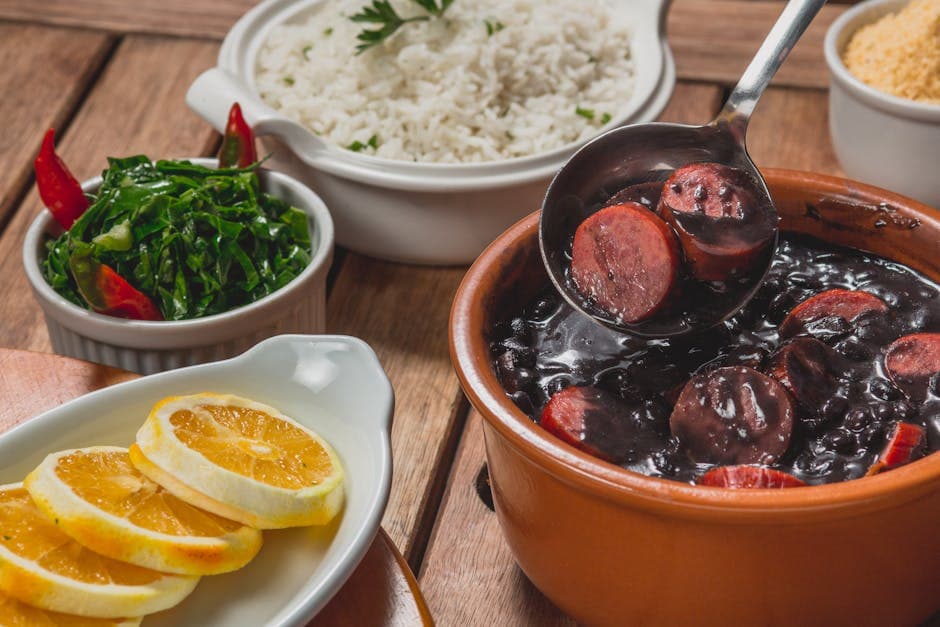 Delicious Brazilian feijoada with rice, greens, and orange slices served on a wooden table.