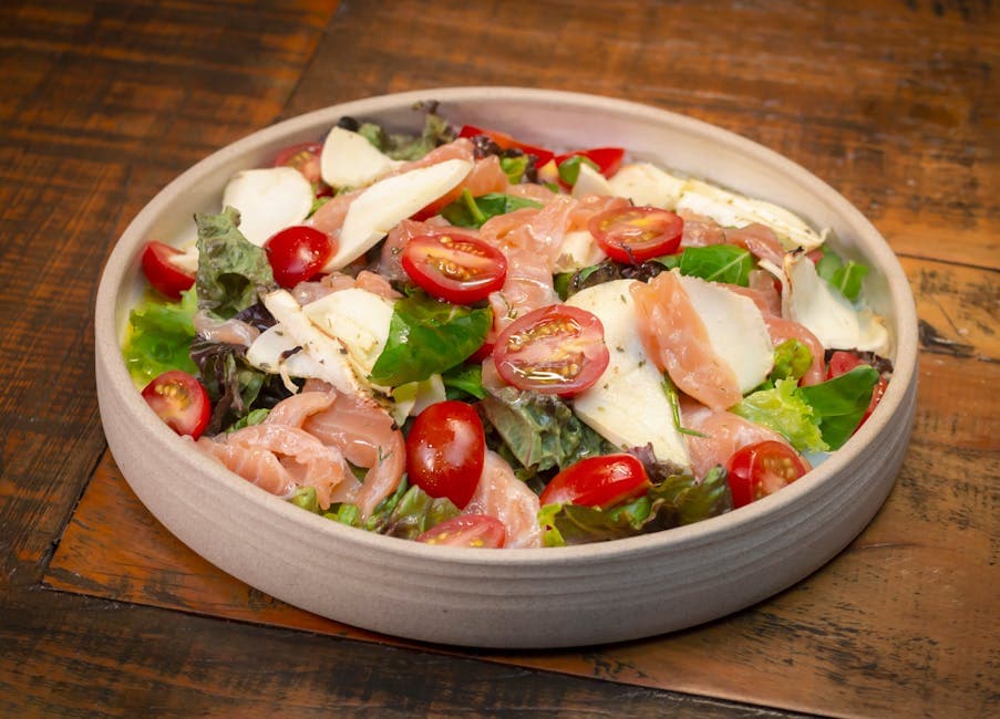 Delicious fresh salad with smoked salmon, mozzarella, and cherry tomatoes on a wooden table.