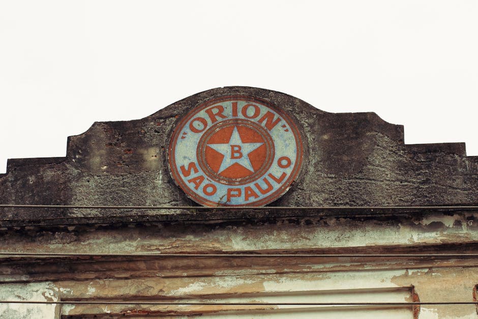 Close-up of a vintage 'Orion' sign on a worn stone building facade in São Paulo.