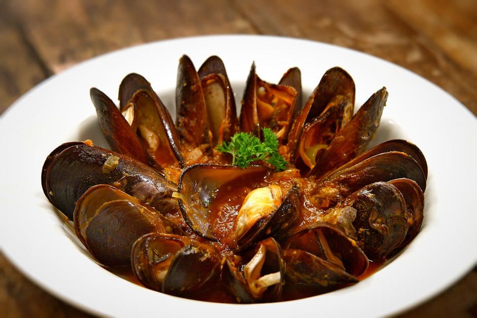 Tasty mussels in a spicy tomato sauce garnished with parsley served in a bowl.