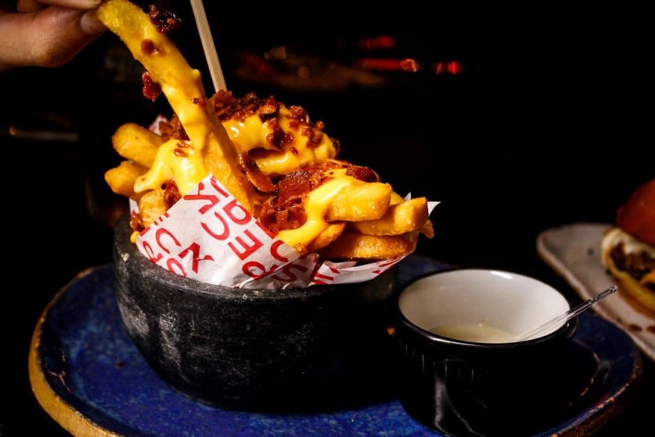 Delicious french fries topped with cheese and bacon served with sauce in a dark setting.