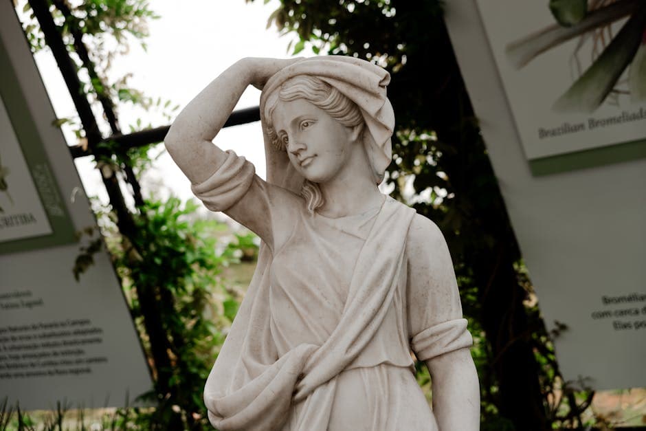 A marble statue of a woman in a classical pose surrounded by lush greenery and signage.